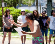 Fernanda Silva aparece em destaque lendo e se movimentando, Público observa de pé.